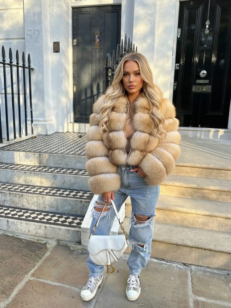 Woman wearing an island fox fur coat and ripped jeans standing on steps outside a building.
