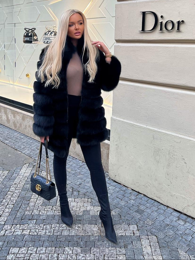 Woman in a blue fox fur coat standing in front of a Dior store.