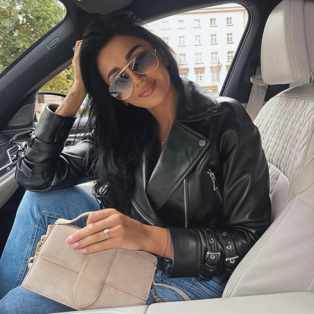 Woman sitting in a car wearing sunglasses and a black leather jacket.